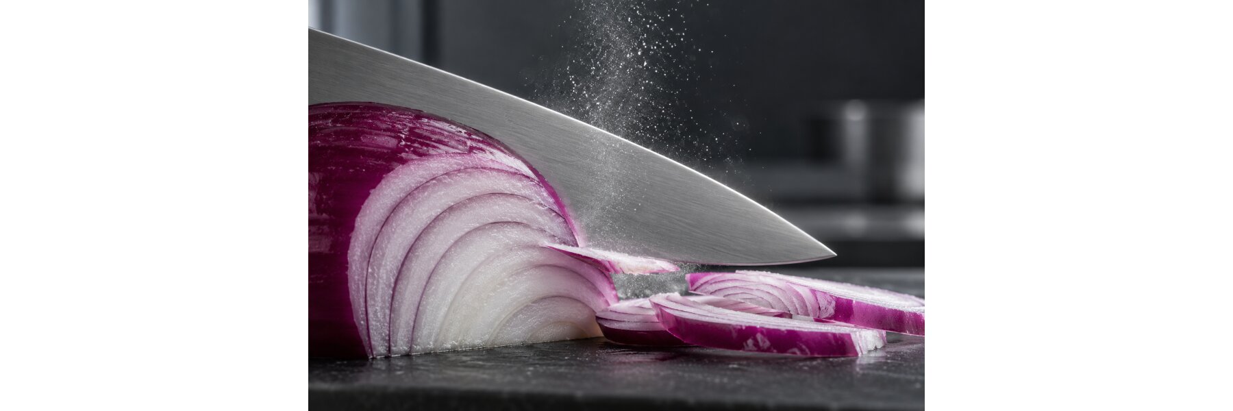 Scharfes Messer beim Schneiden einer roten Zwiebel mit feinen Tröpfchen